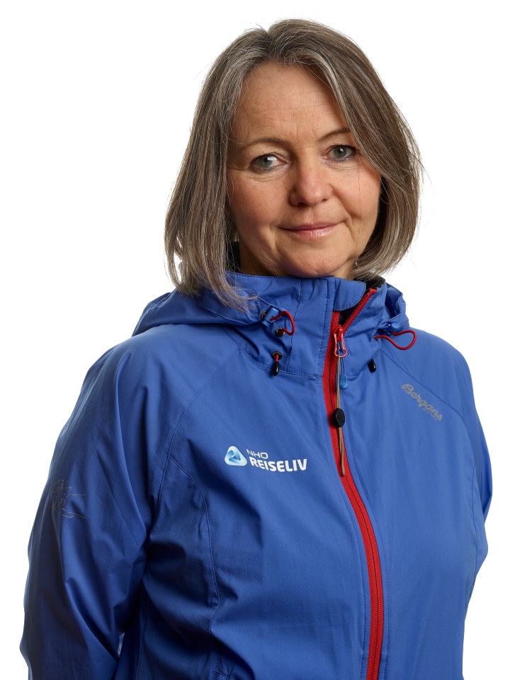 En smilende kvinne med NHO REISELIVs logoen på jakka si. Foto.